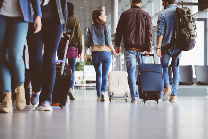 Passengers walking in the airport corridor with luggage.